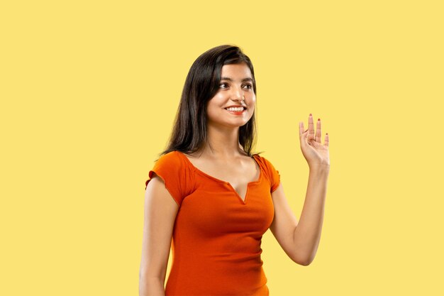 Beautiful female half-length portrait isolated on yellow  space. Young emotional indian woman in dress greeting and inviting. Negative space