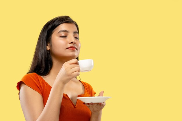 Beautiful female half-length portrait isolated. Young emotional indian woman in dress drinking coffee. Negative space. Facial expression, human emotions concept.