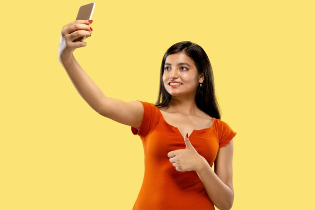 Beautiful female half-length portrait isolated. Young emotional indian woman in dress making selfie. Negative space. Facial expression, human emotions concept.