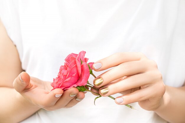 완벽한 황금색과 분홍색 네일 디자인으로 아름다운 여성의 손을 잡고 신선한 장미 꽃