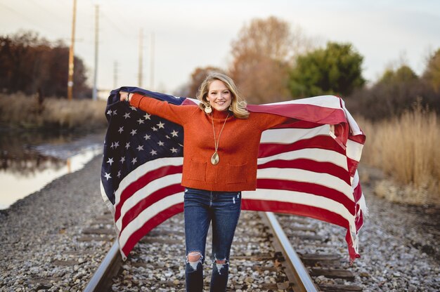 鉄道に立っている間アメリカの国旗を保持している美しい女性