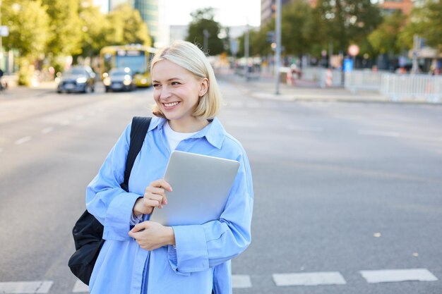 無料写真 青いシャツを着た美しい女性モデルが ⁇ ラップトップコンピュータとバックパックを背負い ⁇ 路上でポーズをとっています ⁇