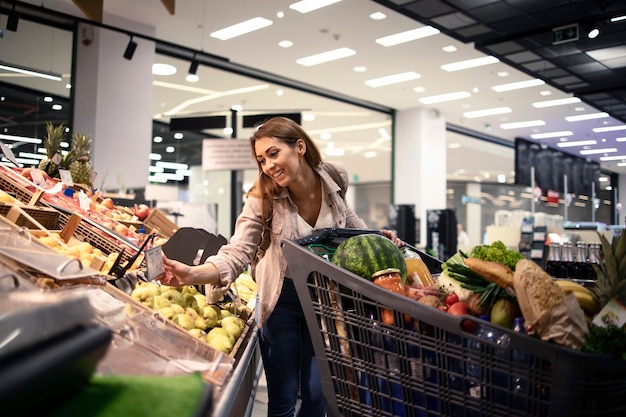 食料品店で果物の価格をチェックする美しい女性