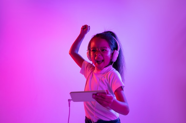 Free photo beautiful female portrait isolated on purple backgroud in neon light. emotional girl in eyeglasses. human emotions, facial expression concept. dancing, listening to music, gaming and winning.