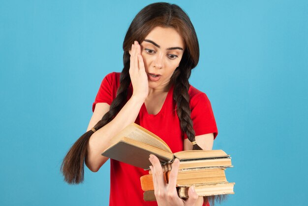 Красивая студентка в красной книге чтения футболки с потрясенным выражением.