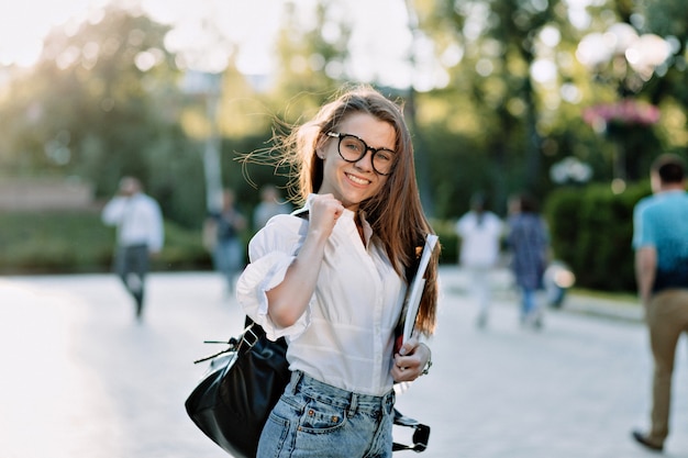 バックパックと屋外の本を持つ美しい女子学生。