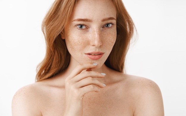 Foto gratuita bella donna femminile e attraente con capelli rossi naturali e lentiggini su viso e corpo che toccano delicatamente il mento con le dita e lo sguardo sensuale e rilassato prendersi cura della bellezza e della pelle