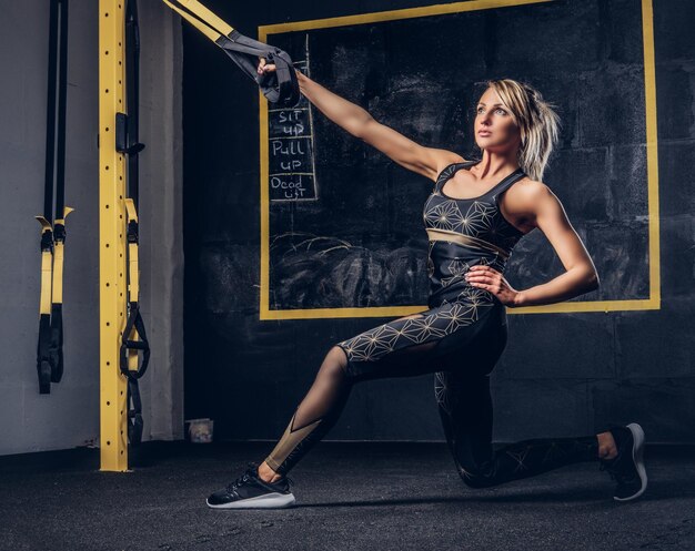 Beautiful fit woman in sportswear doing exercise with suspension straps system at gym.