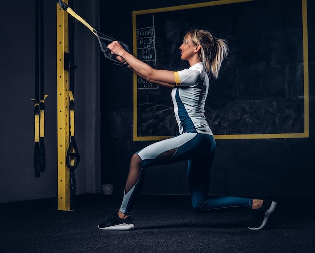 Beautiful fit woman in sportswear doing exercise with suspension straps system at gym.