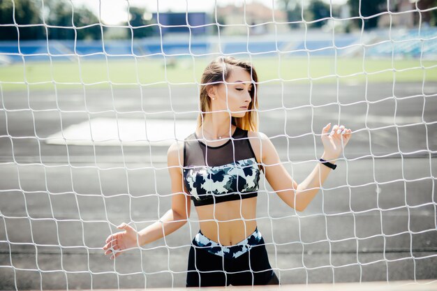 Красивая фитнес женщина в спортивной одежде, позирует возле сетки.
