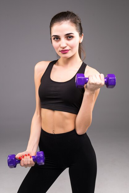 Beautiful fitness woman do toning exercises with dumbbells on gray wall