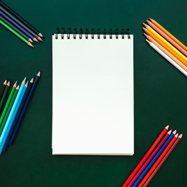 beautiful flat lay composition with notebook with color pencils on green board for back to school