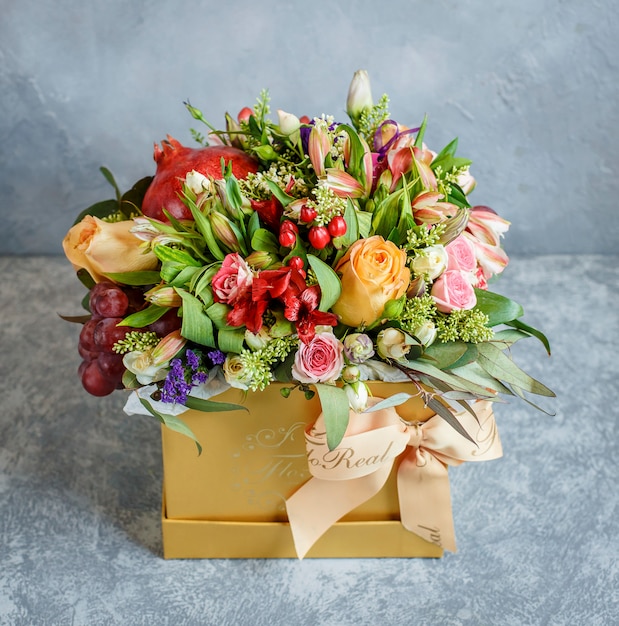 A beautiful flower bouquet with pomegranate and grapes in yellow box with bowtie