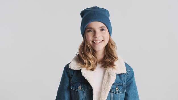 Beautiful friendly blond teenager girl dressed in hat and denim jacket looking cute isolated on white background