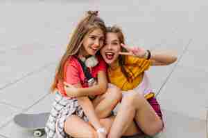 Free photo beautiful friends in trendy colorful attires fooling around while sitting on the ground