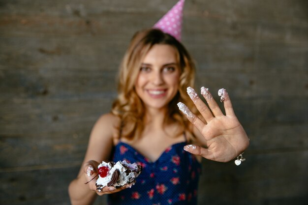 誕生日のケーキを食べた後にクリームの彼女のヤシを示すお祝いの帽子の美しい面白い女の子