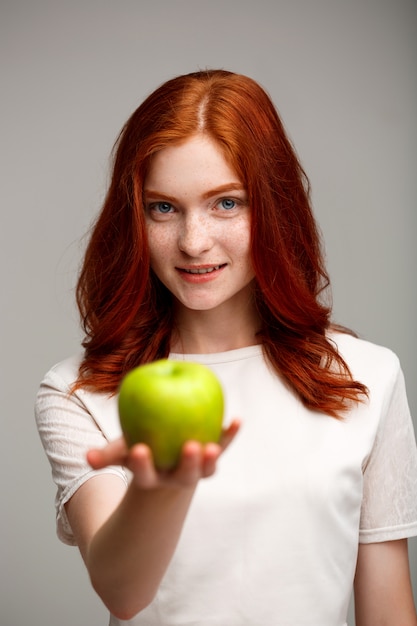 красивая рыжая девочка, держащая яблоко, запятнанное по серой стене.