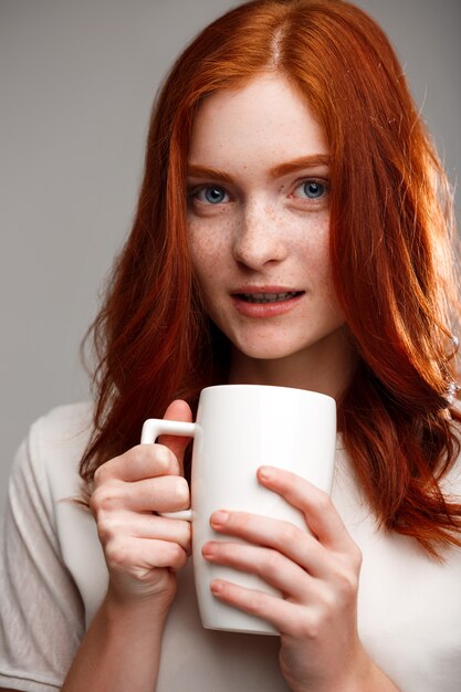 beautiful ginger girl holding cup over gray wall.