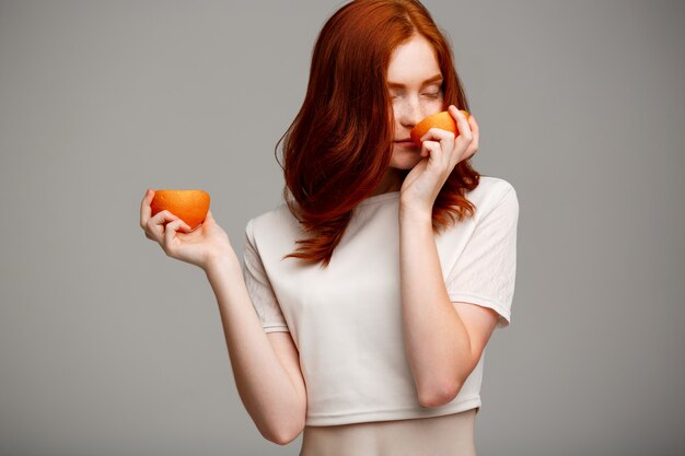 beautiful ginger girl holding oranges over gray wall.