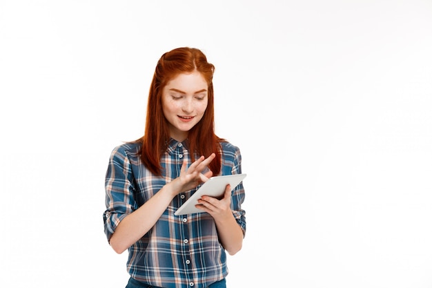 Free photo beautiful ginger girl holding tablet over white wall.