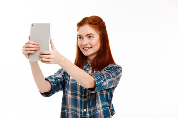  beautiful ginger girl making selfie over white wall.