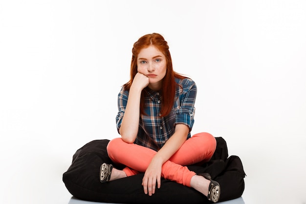 beautiful ginger girl sitting crosslegged over white wall.