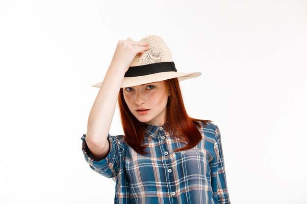 beautiful ginger girl with hat on over white wall.