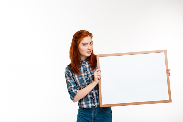 Free photo beautiful ginger girl with whiteboard over white wall.