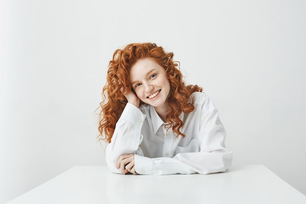 Beautiful ginger woman with curly hair smiling sitting at table.