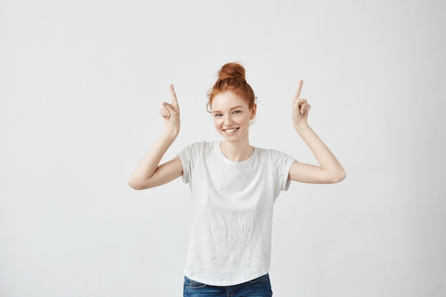 Beautiful ginger woman with freckles smiling pointing fingers up.