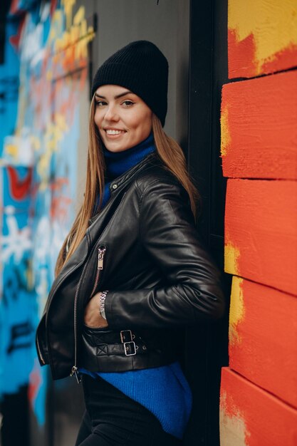 Beautiful girl in black jacket standing by colorful wall