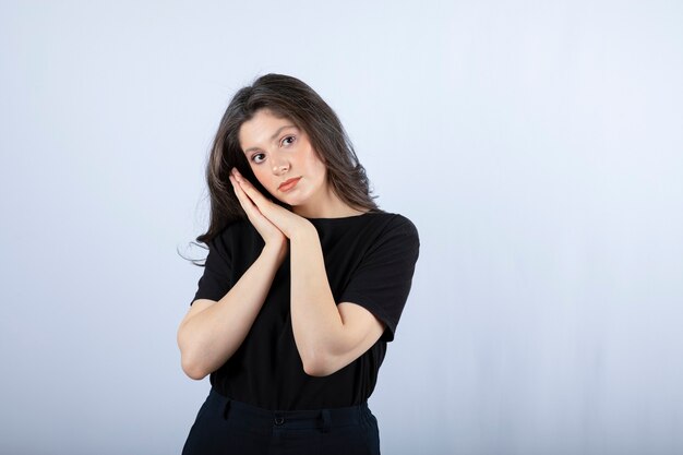 Beautiful girl in black outfit posing to camera on white wall. 