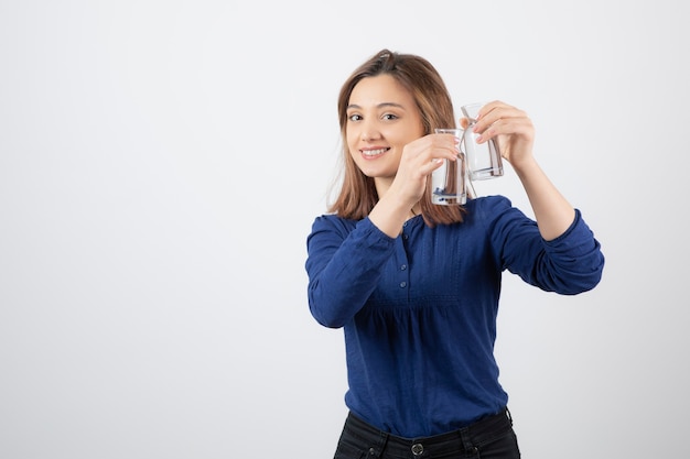 Beautiful girl in blue blouse holding glass of water on white.