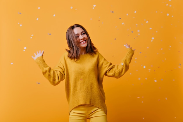 Free photo beautiful girl in bright clothes dancing with pleasure. enthusiastic caucasian lady in yellow sweater fooling around during indoor photoshoot.