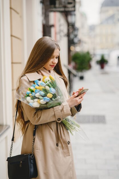 Beautiful girl in a brown coat. Woman in a spring city. Lady with bouquet of flowers