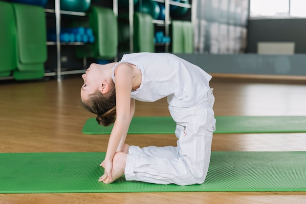 Beautiful girl child practicing camel pose in gym