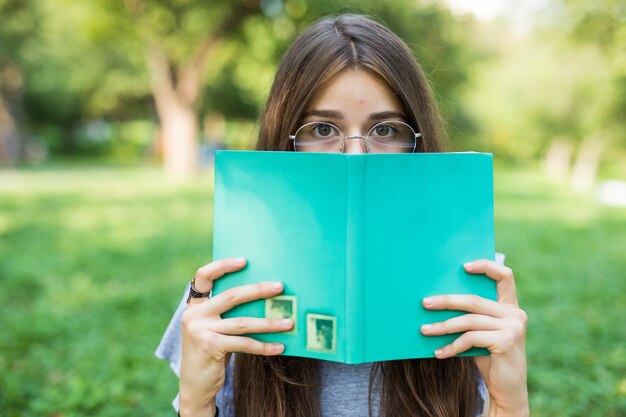 Beautiful girl covering her face with book education and people concept selective focus.