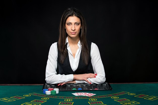 The beautiful girl, dealer, behind a table for game in poker. the dealer deals the cards. He is looking at the camera