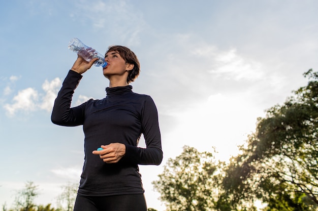 Beautiful girl drinking water from a bottle in the park.