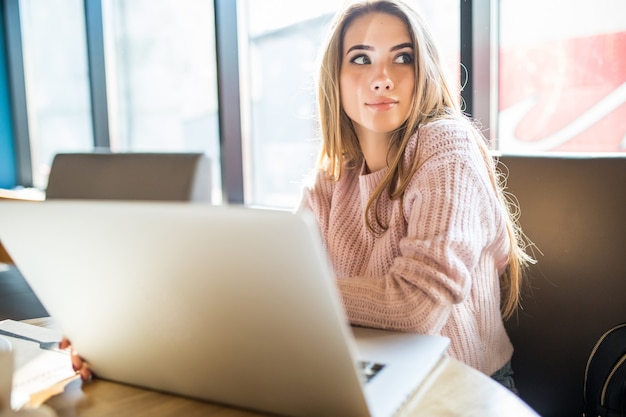 Beautiful girl in fashion white sweater in working on her laptop computer in cafe in daily time