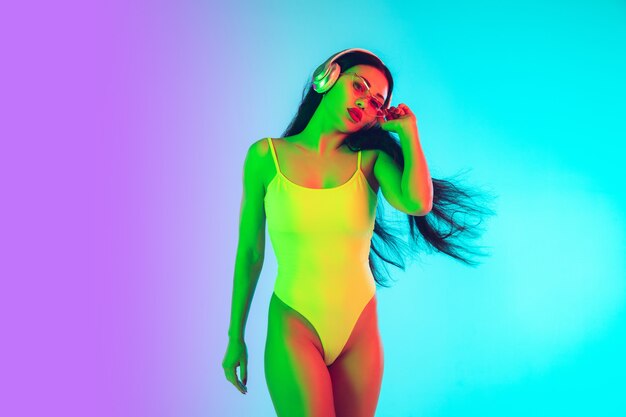 Beautiful girl in fashionable swimsuit isolated on gradient in neon light.