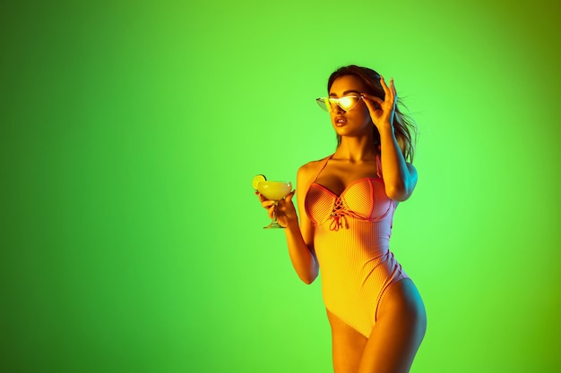 Beautiful girl in fashionable swimsuit isolated on gradient in neon light