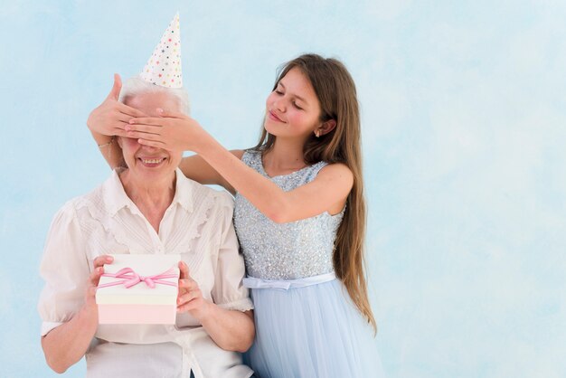 Красивая девушка дает удивленный подарок, закрыв глаза бабушки