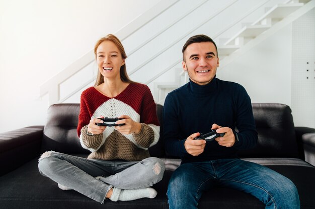 beautiful girl and handsome guy playing video games, sitting on couch together