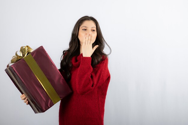 Beautiful girl holding a Christmas present and blowing an air kiss . 