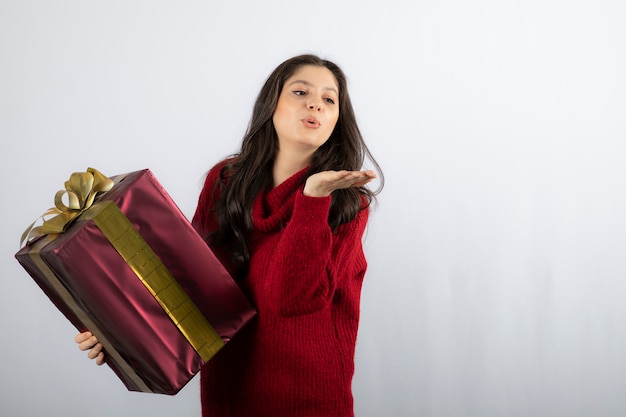 Beautiful girl holding a Christmas present and blowing an air kiss . 