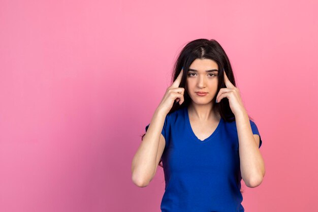 Beautiful girl holding her fingers to her head and thinking on pink background High quality photo