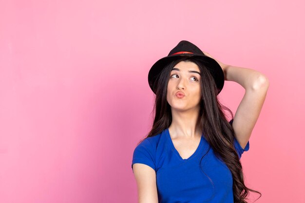 A beautiful girl holding her hand to her hat and looking aside on pink background High quality photo