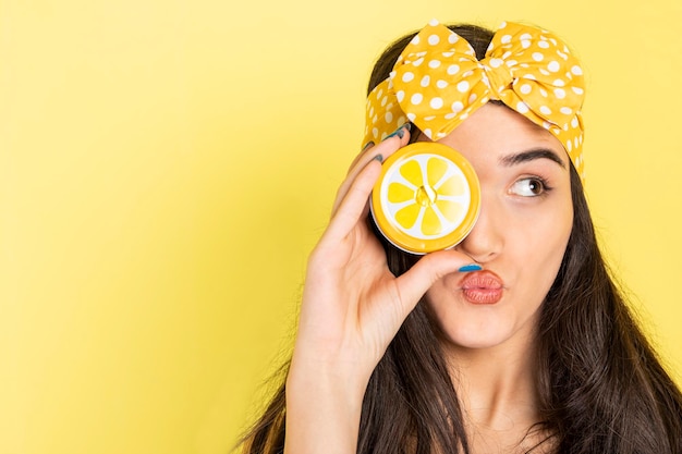 A beautiful girl holding orange slice to her eye and looking aside