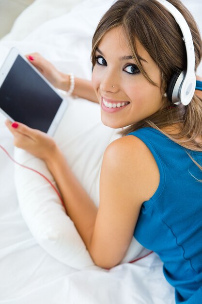 Beautiful girl listening to music with tablet on sofa at home.